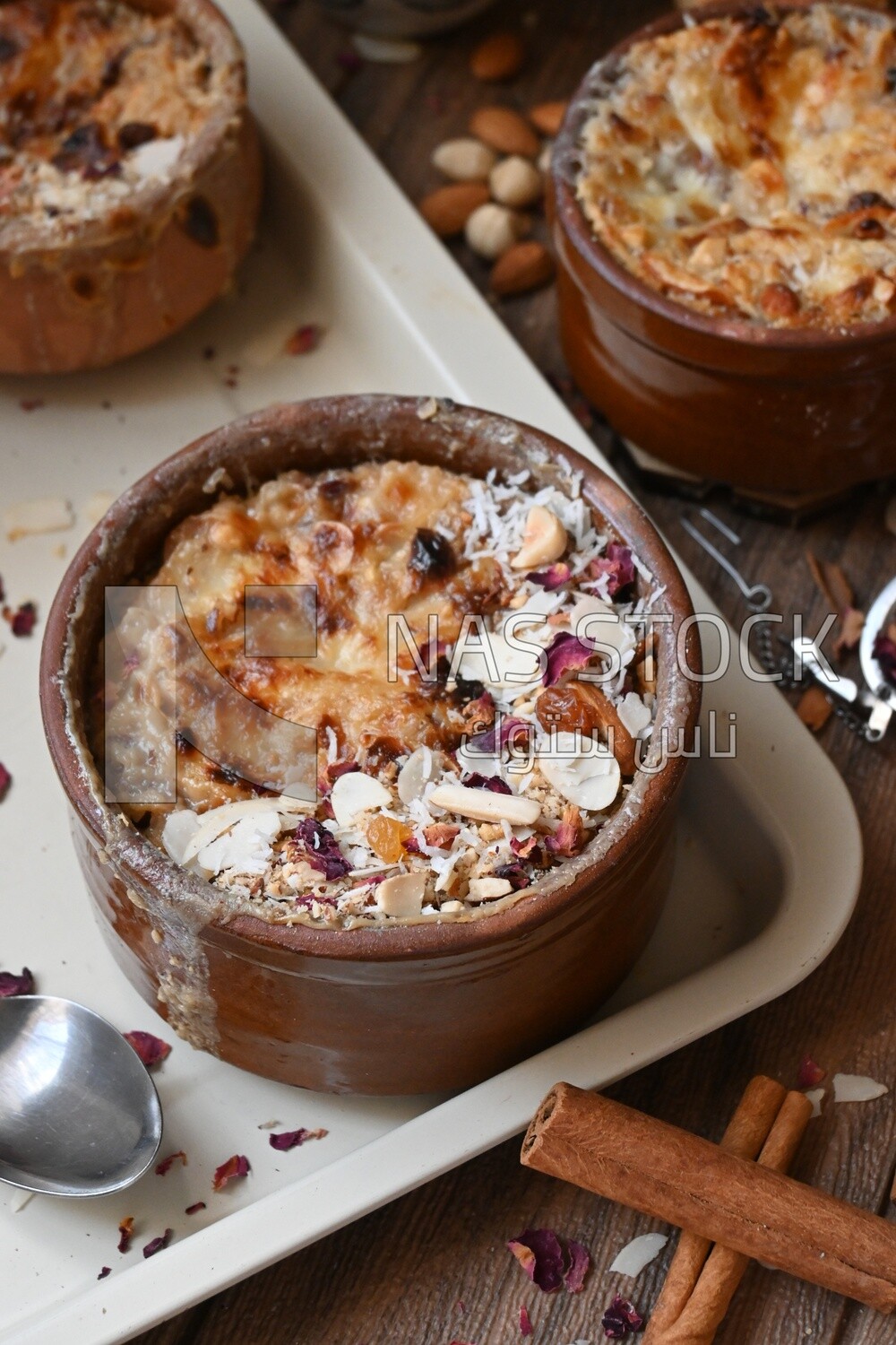 Close up of a plate of Umm Ali with nuts on it, cinnamon sticks, famous oriental Arabic sweets, bread and milk sweets