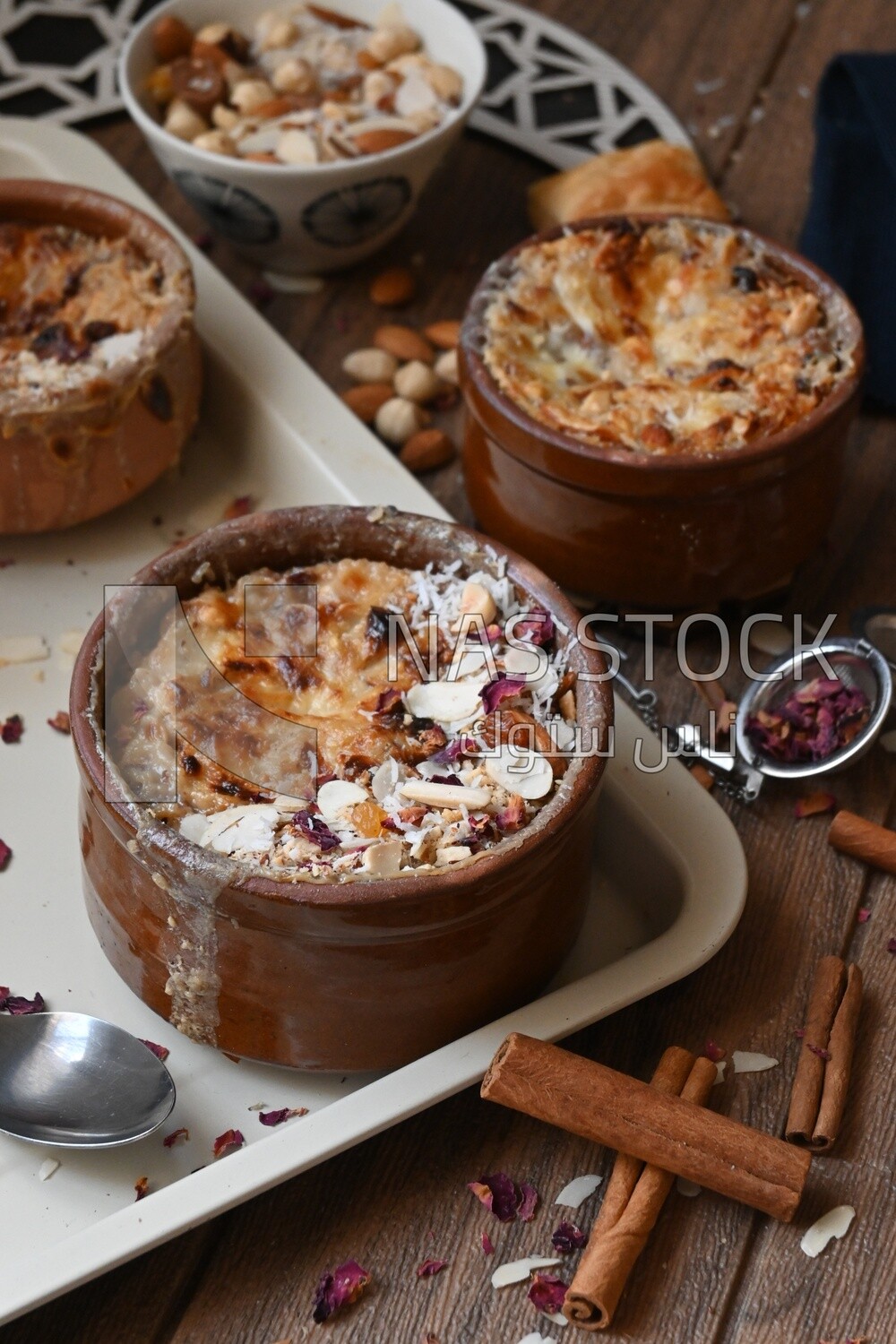 Plate of Umm Ali with nuts on it, cinnamon sticks, famous oriental Arabic sweets, bread and milk sweets