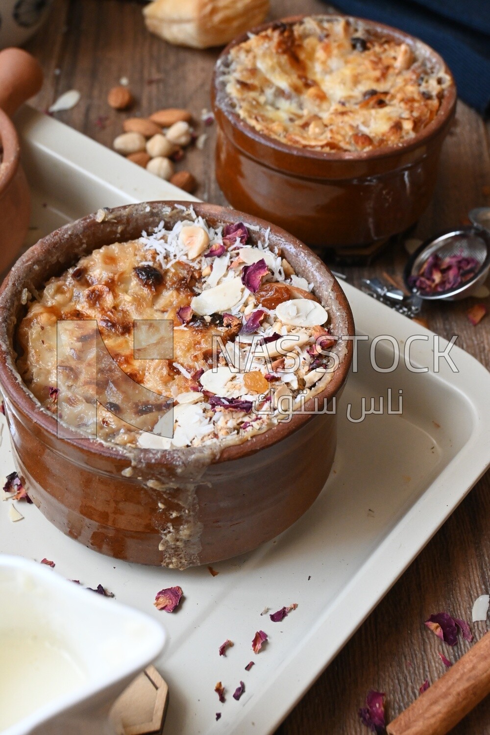 Plate of Umm Ali with nuts on it, cinnamon sticks, famous oriental Arabic sweets, bread and milk sweets