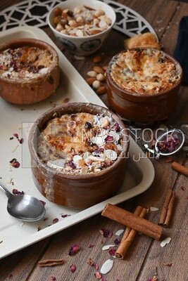 Plate of Umm Ali with nuts on it, cinnamon sticks, famous oriental Arabic sweets, bread and milk sweets