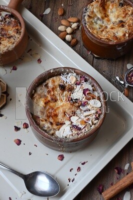 Plate of Umm Ali with nuts on it, cinnamon sticks, famous oriental Arabic sweets, bread and milk sweets