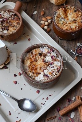 Top view of a plate of Umm Ali with nuts on it, cinnamon sticks, famous oriental Arabic sweets, bread and milk sweets