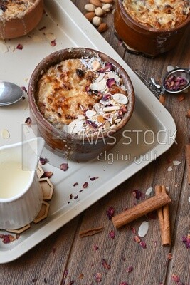Plate of Umm Ali with nuts on it, cinnamon sticks, famous oriental Arabic sweets, bread and milk sweets