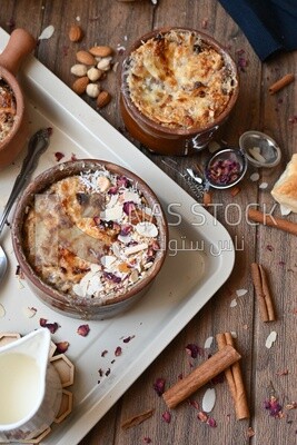 Plate of Umm Ali with nuts on it, cinnamon sticks, famous oriental Arabic sweets, bread and milk sweets