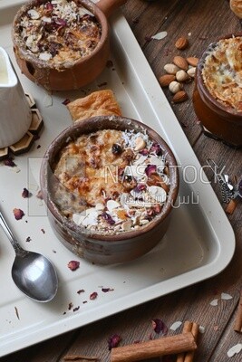 Top view of a plate of Umm Ali with nuts on it, cinnamon sticks, famous oriental Arabic sweets, bread and milk sweets
