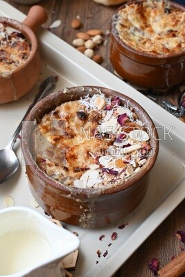 Plate of Umm Ali with nuts on it, cinnamon sticks, famous oriental Arabic sweets, bread and milk sweets