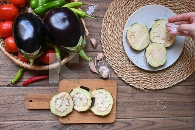 Hand puts the salt on the eggplant before cooking