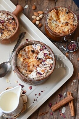 Top view of a plate of Umm Ali with nuts on it, cinnamon sticks, famous oriental Arabic sweets, bread and milk sweets