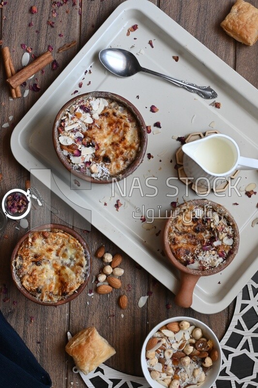 Top view of a plate of Umm Ali with nuts on it, cinnamon sticks, famous oriental Arabic sweets, bread and milk sweets