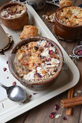 Top view of a plate of Umm Ali with nuts on it, cinnamon sticks, famous oriental Arabic sweets, bread and milk sweets