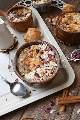 Plate of Umm Ali with nuts on it, cinnamon sticks, famous oriental Arabic sweets, bread and milk sweets