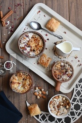 Top view of a plate of Umm Ali with nuts on it, cinnamon sticks, famous oriental Arabic sweets, bread and milk sweets