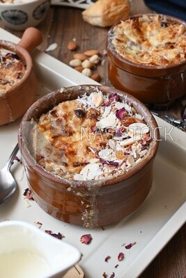 Close up of a plate of Umm Ali with nuts on it, cinnamon sticks, famous oriental Arabic sweets, bread and milk sweets