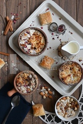 Top view of a plate of Umm Ali with nuts on it, cinnamon sticks, famous oriental Arabic sweets, bread and milk sweets