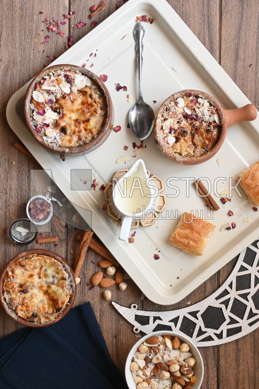 Top view of a plate of Umm Ali with nuts on it, cinnamon sticks, famous oriental Arabic sweets, bread and milk sweets