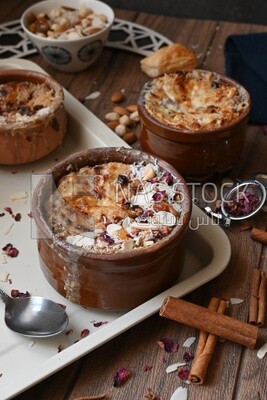 Plate of Umm Ali with nuts on it, cinnamon sticks, famous oriental Arabic sweets, bread and milk sweets