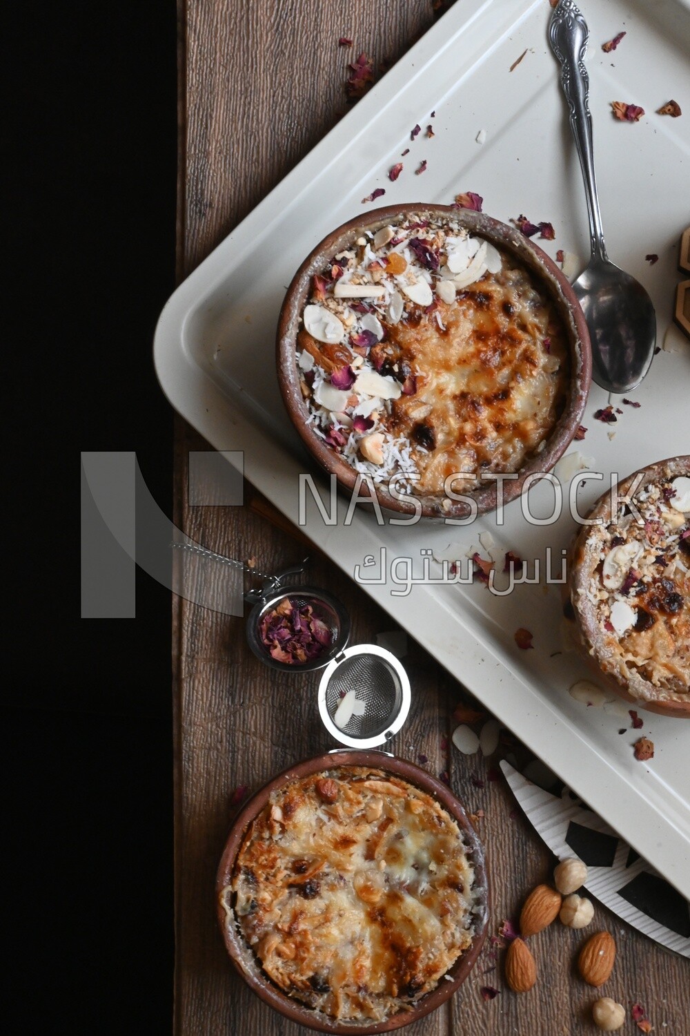 Top view of a plate of Umm Ali with nuts on it, cinnamon sticks, famous oriental Arabic sweets, bread and milk sweets