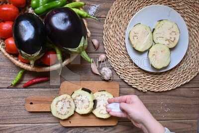 Hand puts the salt on the eggplant before cooking
