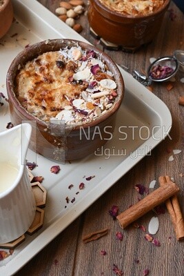 Plate of Umm Ali with nuts on it, cinnamon sticks, famous oriental Arabic sweets, bread and milk sweets