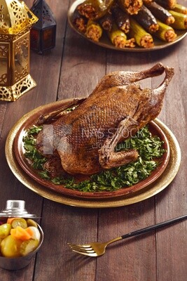 Side view of a scene from a dish containing roast duck with parsley and  different types of stuffed vegetables