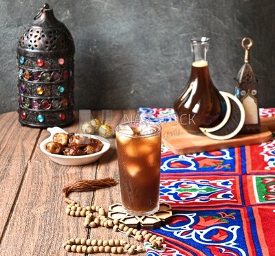 Cup of licorice juice with ice beside a plate of dates, ramadan juice