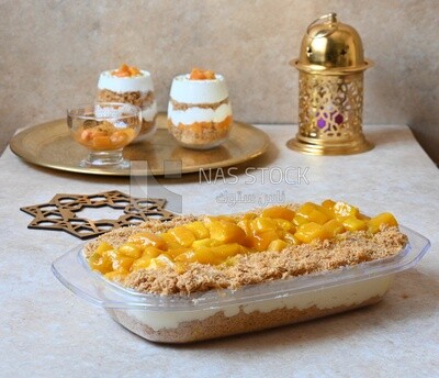 Tray of kunafa with mango and cream beside two cups of kunafa with mango and cream, Ramadan sweets