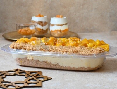 Tray of kunafa with mango and cream beside two cups of kunafa with mango and cream, Ramadan sweets