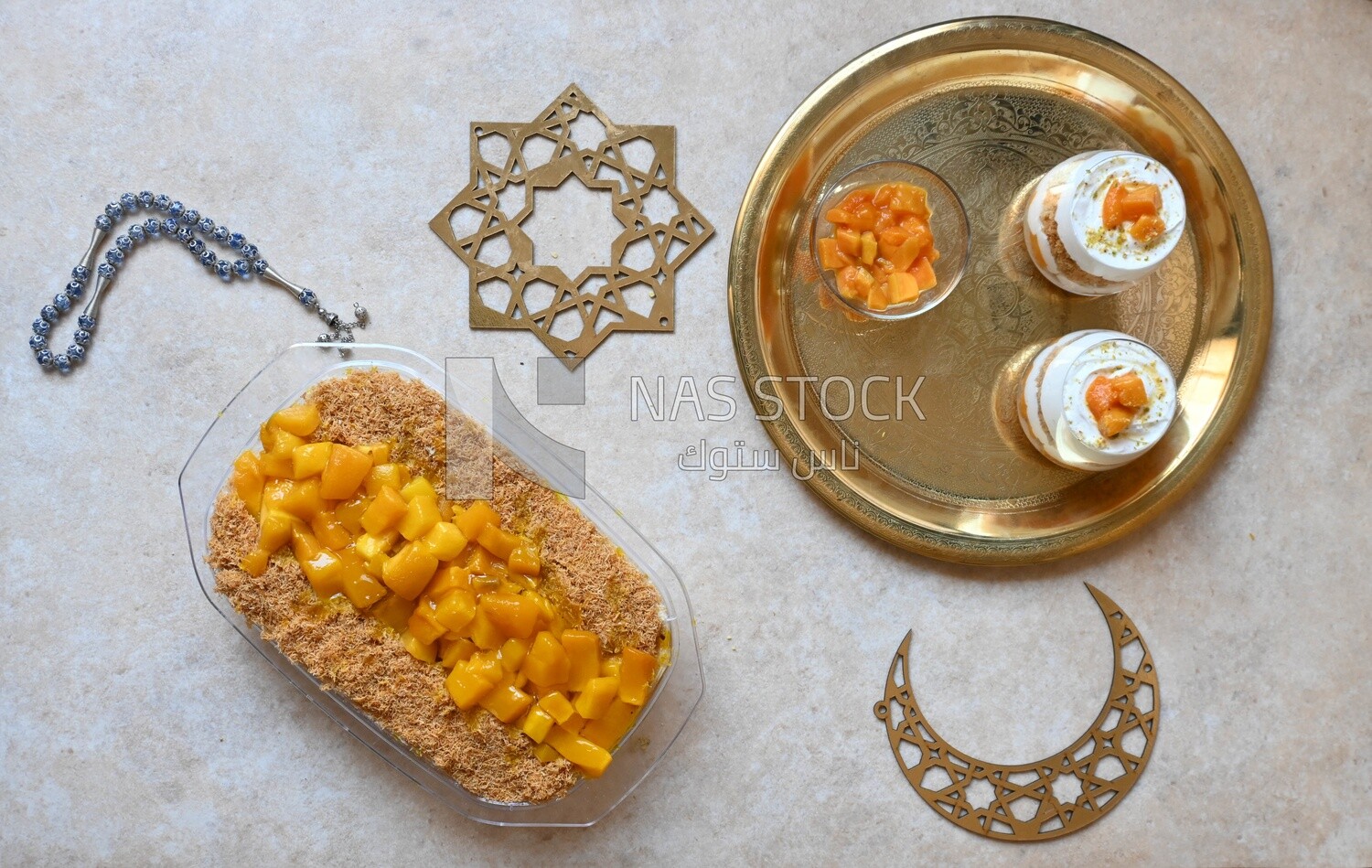 Tray of kunafa with mango and cream beside two cups of kunafa with mango and cream, Ramadan sweets