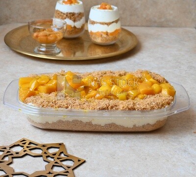 Tray of kunafa with mango and cream beside two cups of kunafa with mango and cream, Ramadan sweets