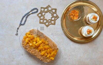 Tray of kunafa with mango and cream beside two cups of kunafa with mango and cream, Ramadan sweets