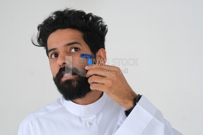 Saudi man holding a razor blade, removing facial hair, skin care and hygiene, shaving his beard, self-care, Saudi model, white background