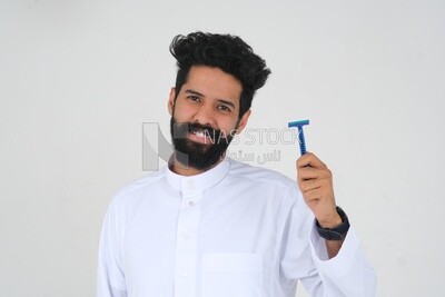 رجل سعودي يحمل شفرة حلاقة ، يزيل شعر الوجه ، العناية بالبشرة والنظافة ، يحلق لحيته ، العناية الذاتية ، موديل سعودى ، خلفية بيضاء
