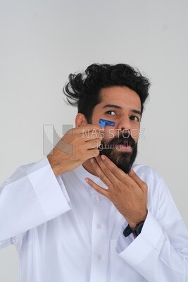 Saudi man holding a razor blade, removing facial hair, skin care and hygiene, shaving his beard, self-care, Saudi model, white background