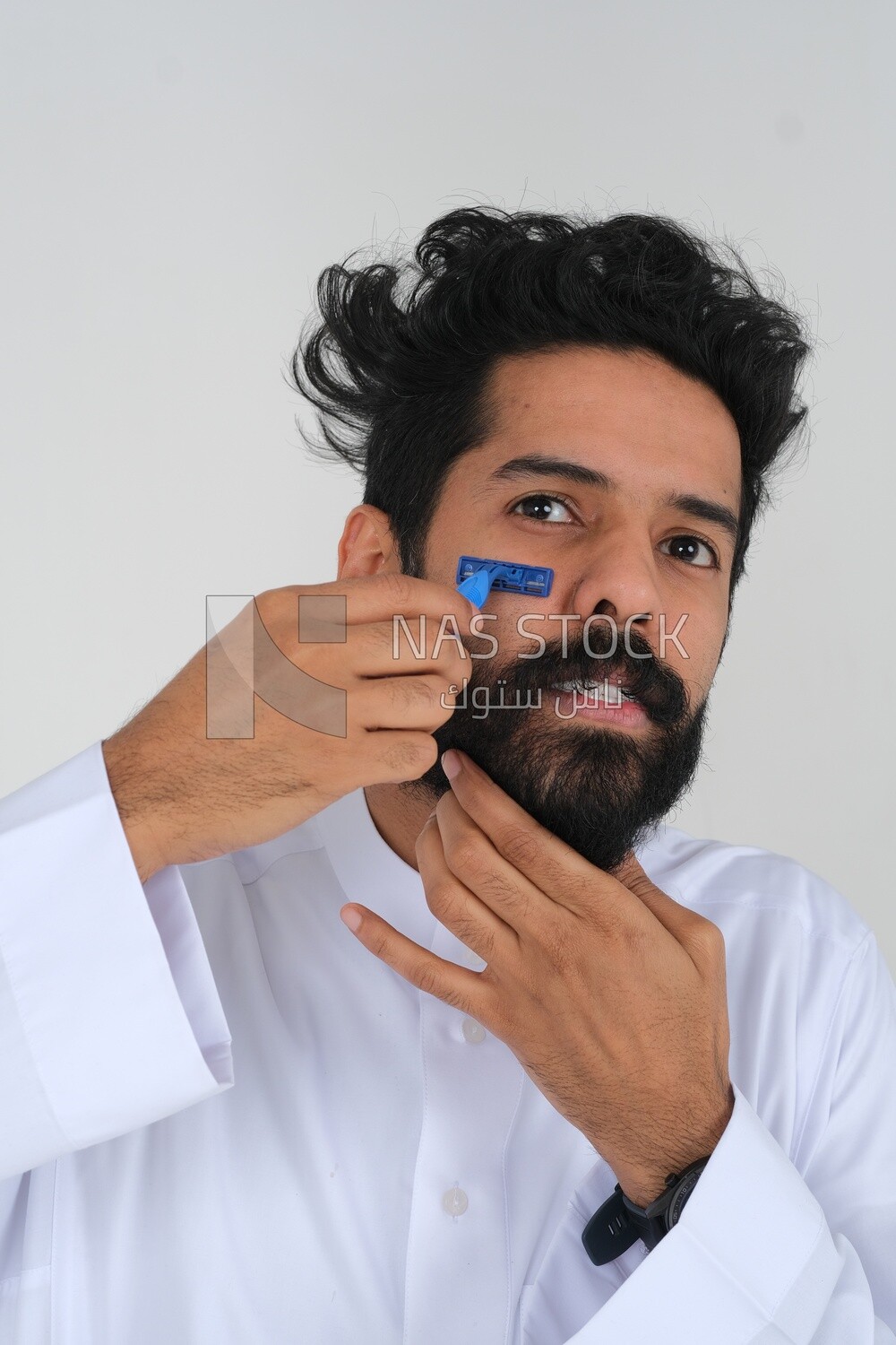 Saudi man holding a razor blade, removing facial hair, skin care and hygiene, shaving his beard, self-care, Saudi model, white background