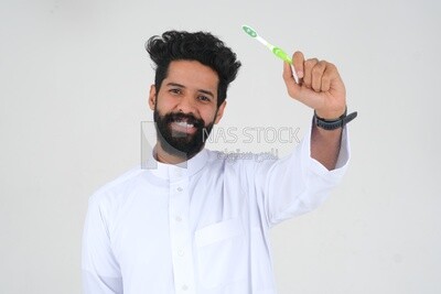 رجل سعودي يحمل فرشاة الأسنان ، ينظف أسنانه بمعجون الأسنان ، العناية بالبشرة والنظافة ، الرعاية الذاتية ، موديل سعودى ، الخلفية البيضاء