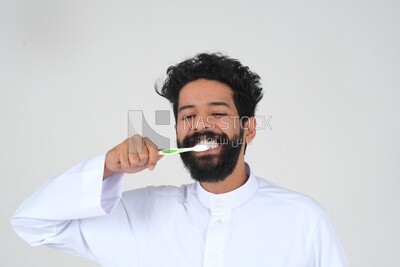 رجل سعودي يحمل فرشاة الأسنان ، ينظف أسنانه بمعجون الأسنان ، العناية بالبشرة والنظافة ، الرعاية الذاتية ، موديل سعودى ، الخلفية البيضاء