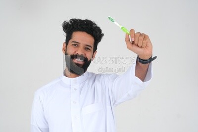Saudi man holding a toothbrush, brushing his teeth with toothpaste, skincare and hygiene, self-care, Saudi model, white background