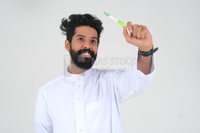 Saudi man holding a toothbrush, brushing his teeth with toothpaste, skincare and hygiene, self-care, Saudi model, white background