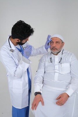 Saudi man wearing a medical coat and a stethoscope, checking the patient&#39;s eyes, white background, medicine and health care, Saudi model
