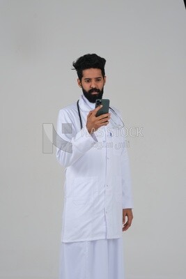Saudi man wearing a medical coat and a stethoscope, using his mobile, white background, medicine and health care, Saudi model