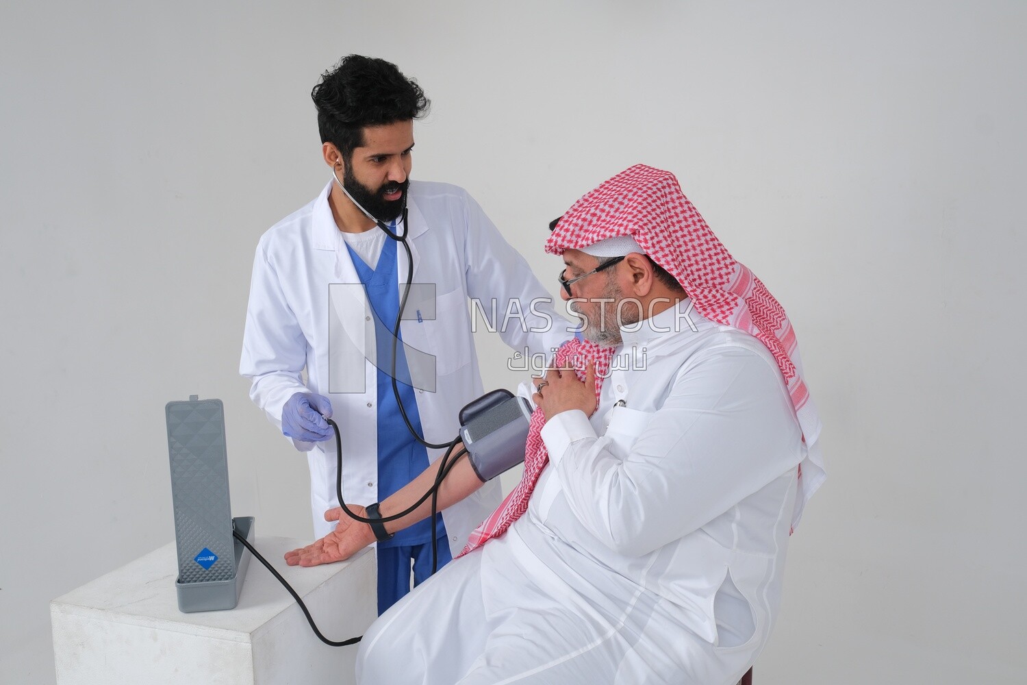 Saudi man wearing a medical coat and a stethoscope, measuring patient pressure, white background, medicine and health care, Saudi model