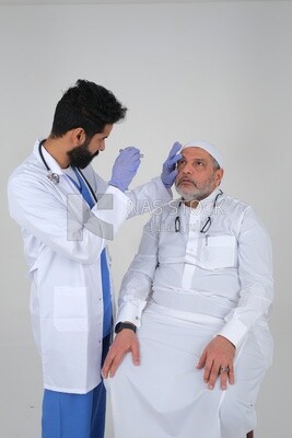 Saudi man wearing a medical coat and a stethoscope, checking the patient&#39;s eyes, white background, medicine and health care, Saudi model
