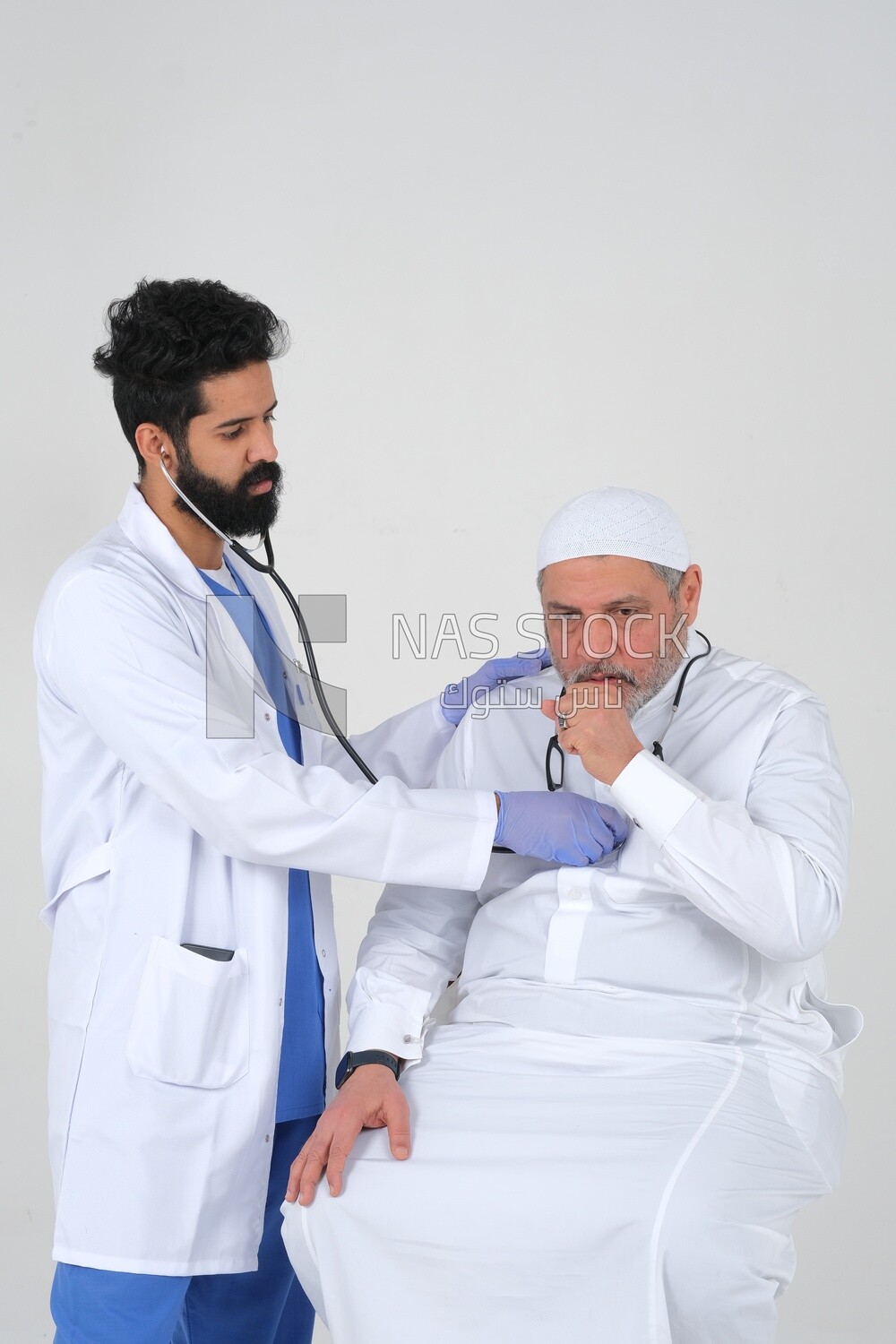 Saudi man wearing a medical coat and a stethoscope, the doctor listens to the patient&#39;s heartbeat, white background, medicine and health care, Saudi model