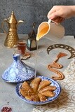 Plate of Qatayef and hand holding a sherbet jug put on Qatayef, oriental Arabic sweets, Ramadan sweets