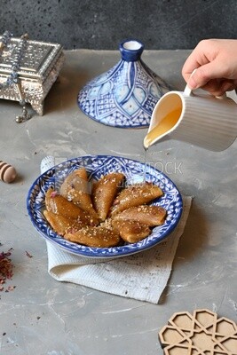 Plate of Qatayef and hand holding a sherbet jug put on Qatayef, oriental Arabic sweets, Ramadan sweets