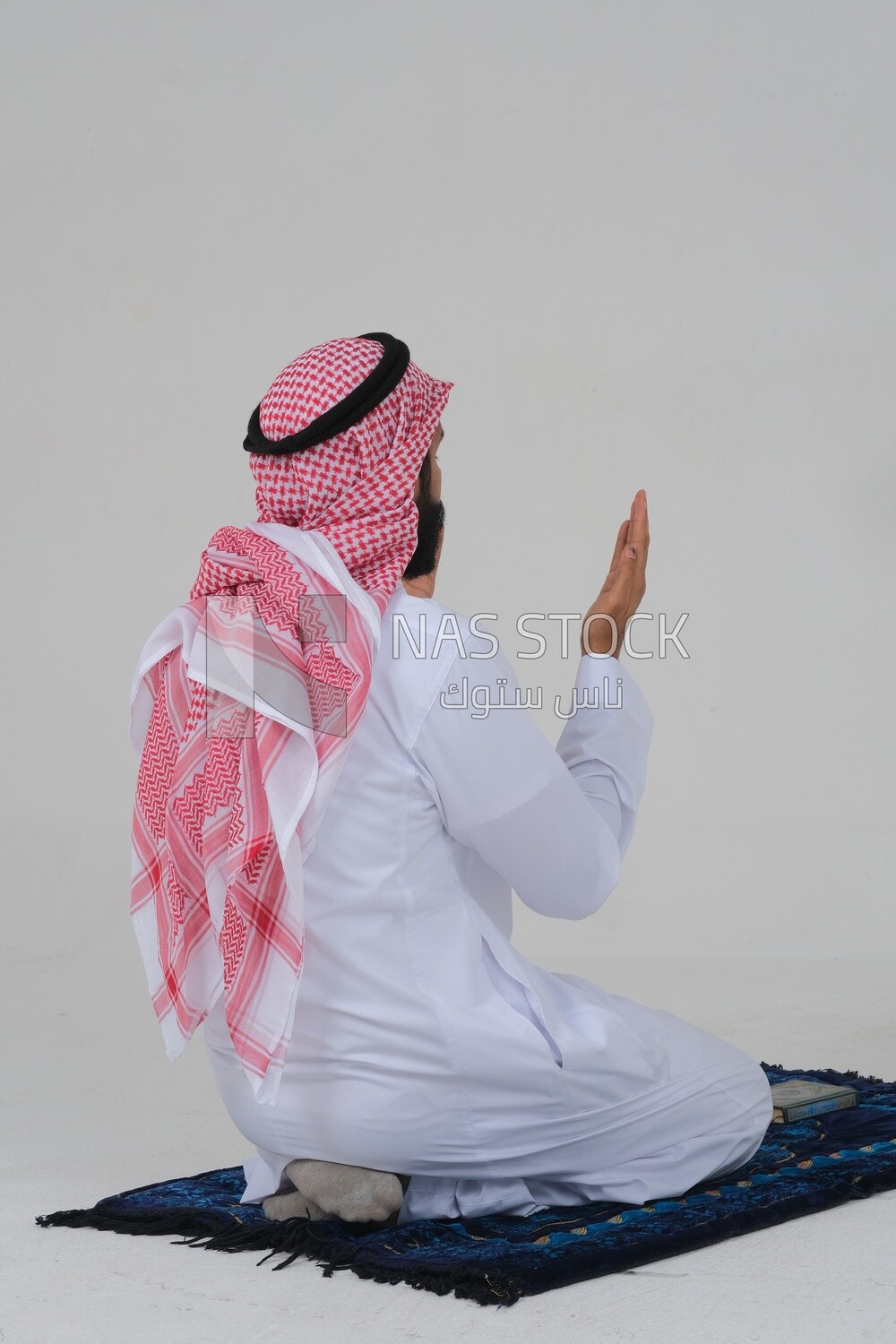 Back of a Saudi man wearing a white dress sitting on the prayer rug, praying to god, praying on the prayer rug, Islam and worship, white background, Saudi model