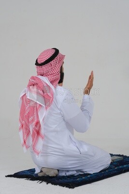 Back of a Saudi man wearing a white dress sitting on the prayer rug, praying to god, praying on the prayer rug, Islam and worship, white background, Saudi model