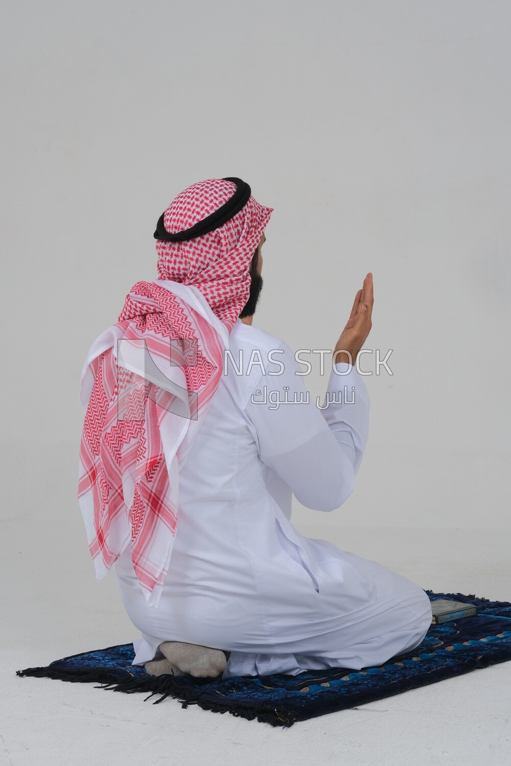 Back of a Saudi man wearing a white dress sitting on the prayer rug, praying to god, praying on the prayer rug, Islam and worship, white background, Saudi model