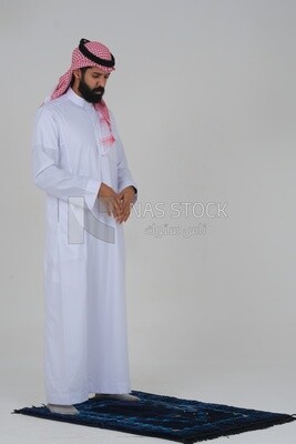 Side view of a Saudi man wearing a white dress sitting on the prayer rug, praying to god, praying on the prayer rug, Islam and worship, white background, Saudi model