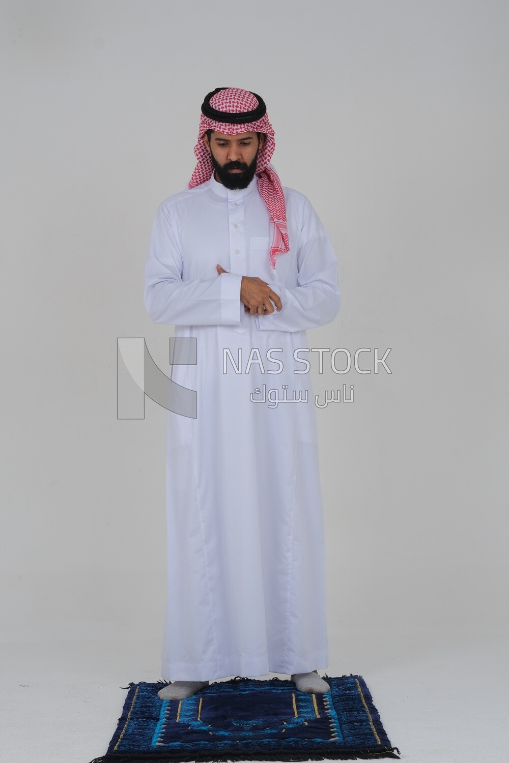 Saudi man wearing a white thobe and shemagh praying on the prayer rug, praying to god, Islam and worship, white background, Saudi model